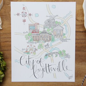 May include: A hand-drawn map of the city of Fayetteville, North Carolina. The map features landmarks like the courthouse, the old bridge, and the First Presbyterian Church. The map is drawn in a whimsical style with watercolor washes and black ink.