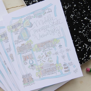 May include: A white paper print featuring a hand-drawn map of Middle Tennessee State University with blue paths and green trees. The illustration includes labeled campus buildings like the library and stadium, with cursive text at the top right.