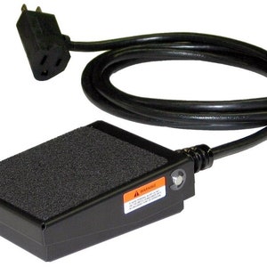 May include: Black foot pedal switch with a black power cord and a standard three-prong plug. The pedal has a textured surface and a warning label.