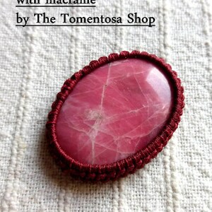 Pode incluir: Close-up de um caboch&atilde;o rosa envolto em cord&atilde;o de macram&eacute; marrom. O caboch&atilde;o tem um padr&atilde;o de m&aacute;rmore e &eacute; cercado por um cord&atilde;o grosso. A imagem est&aacute; sobre um fundo de tecido branco. O texto "How to wrap a cabochon with macrame by The Tomentosa Shop" est&aacute; na parte superior da imagem. O texto "Step by step PDF photo Tutorial" est&aacute; na parte inferior da imagem.