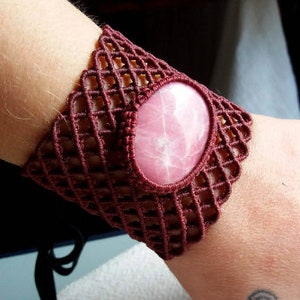 May include: A maroon crocheted bracelet with a pink gemstone in the center.