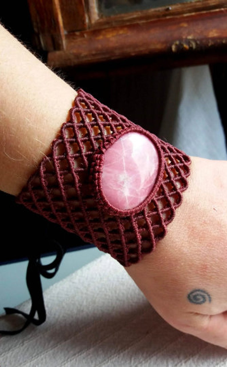 May include: A maroon crocheted bracelet with a pink gemstone in the center.