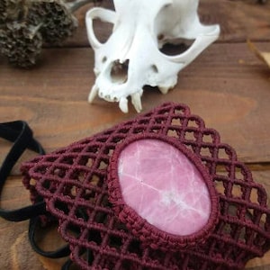 May include: A burgundy crocheted bracelet with a pink stone in the center. The bracelet is made with a grid pattern and has a delicate, feminine look.