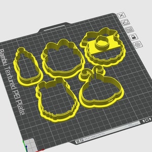 Peut inclure: Un ensemble de cinq emporte-pi&egrave;ces en plastique jaune sur une surface textur&eacute;e grise. Les emporte-pi&egrave;ces sont en forme de bouteille, de fleur, de couronne, de citrouille et d'ours.