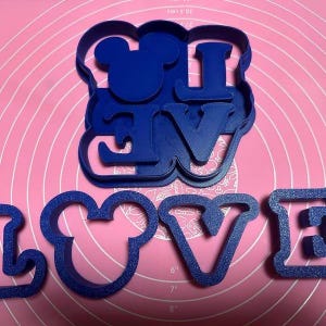 Peut inclure: Emporte-pi&egrave;ces en plastique bleu en forme des lettres "LOVE" avec une t&ecirc;te de Mickey Mouse &agrave; la place du "O".