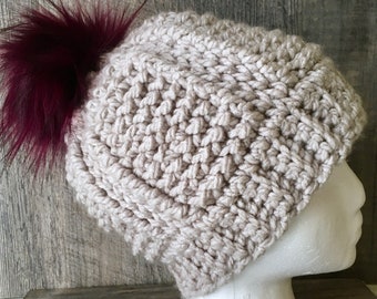 May include: A beige crocheted beanie with a burgundy faux fur pom pom.