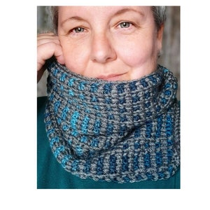 Könnte beinhalten: Ein grauer und blauer Häkel-Kragenwärmer. Der Kragenwärmer ist mit einem strukturierten Stichmuster gearbeitet.