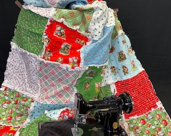 May include: A colorful Christmas-themed quilt with a patchwork design, featuring red, green, and blue squares with holiday patterns. A vintage black Singer sewing machine sits on the quilt, adding a touch of nostalgia.