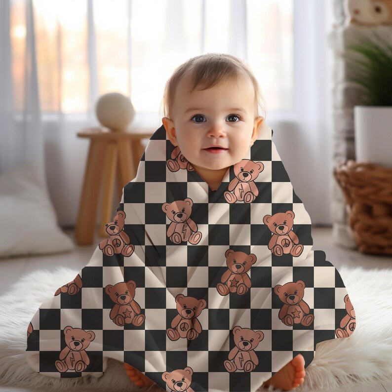 Pu&ograve; includere: Un bambino che indossa una copertina per neonati a scacchi bianchi e neri con un motivo di orsacchiotto di peluche marrone. La copertina ha un orsacchiotto di peluche marrone con un fulmine sul petto su ogni quadrato.