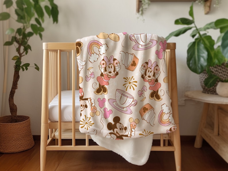 May include: A white and pink baby blanket with a Minnie Mouse theme. The blanket features Minnie Mouse in different poses, along with teacups, donuts, and rainbows.