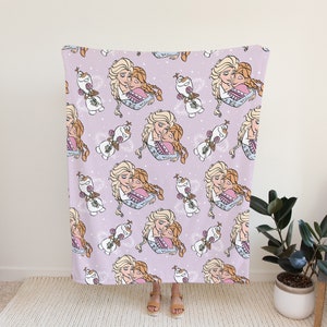 Pu&ograve; includere: Una coperta in pile viola con un motivo ripetuto di due ragazze che si abbracciano e un pupazzo di neve. Le ragazze hanno capelli lunghi biondi e castani e indossano abiti blu. Il pupazzo di neve &egrave; bianco con un naso di carota e occhi neri.