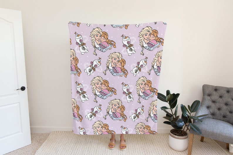 Pu&ograve; includere: Una coperta in pile viola con un motivo ripetuto di due ragazze che si abbracciano e un pupazzo di neve. Le ragazze hanno capelli lunghi biondi e castani e indossano abiti blu. Il pupazzo di neve &egrave; bianco con un naso di carota e occhi neri.