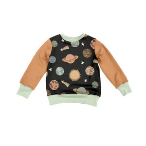 May include: A black long-sleeved sweatshirt with a mint green trim. The sweatshirt has a pattern of planets, stars, and a comet on the front.