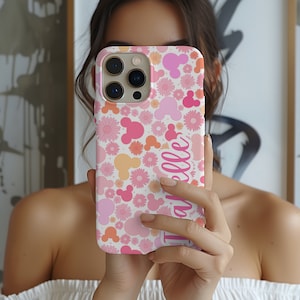 May include: A white phone case with a pink and yellow floral pattern and pink Mickey Mouse heads. The name "Isabelle" is written in pink on the case.