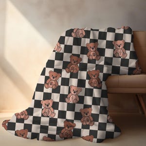 Pu&ograve; includere: Una coperta a quadri bianchi e neri con un motivo ripetuto di orsacchiotti marroni che indossano simboli di pace. La coperta &egrave; morbida e accogliente, perfetta per coccolarsi sul divano.