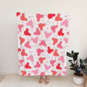 May include: A white throw blanket with a repeating pattern of pink and red Mickey Mouse head balloons with black outlines and small hearts.