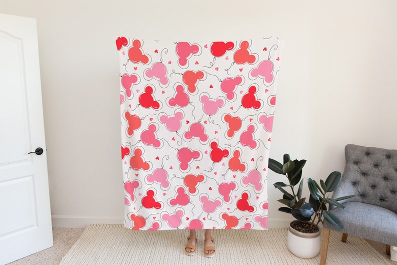 May include: A white throw blanket with a repeating pattern of pink and red Mickey Mouse head balloons with black outlines and small hearts.