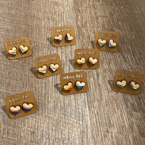 May include: Eight pairs of rainbow heart-shaped wooden earrings on brown card stock with the text "Nona Rae" printed on each card.