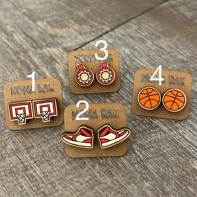 May include: Four pairs of wooden earrings with a basketball theme. The earrings feature basketballs, basketball shoes, basketball hoops, and basketballs with red and white accents. The earrings are labeled with numbers 1 through 4.