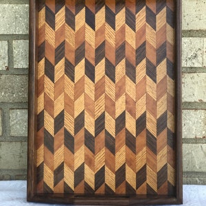 May include: A wooden serving tray with a herringbone pattern made from different types of wood. The tray has a dark brown border and a light brown interior.
