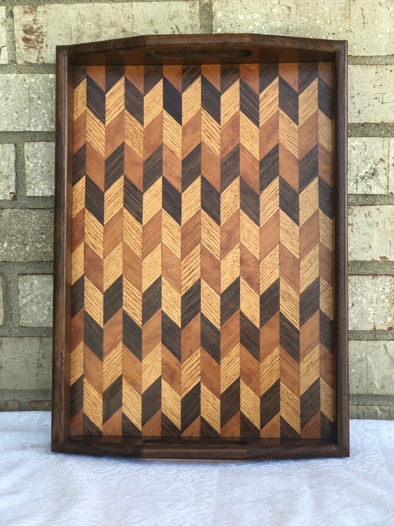 May include: A wooden serving tray with a herringbone pattern made from different types of wood. The tray has a dark brown border and a light brown interior.