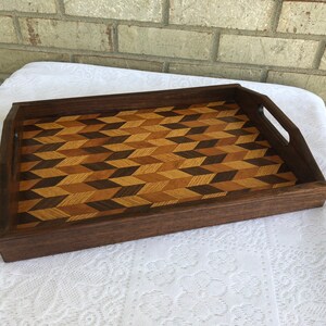 May include: A wooden serving tray with a geometric pattern inlay. The tray is made of dark wood and has two handles on the sides.
