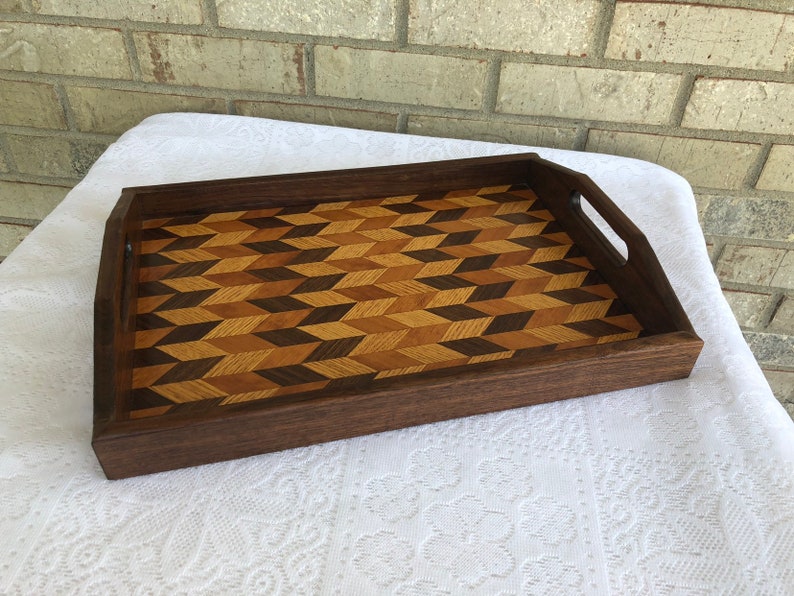 May include: A wooden serving tray with a geometric pattern inlay. The tray is made of dark wood and has two handles on the sides.