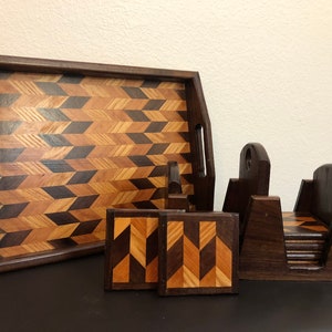 May include: A set of wooden coasters and a serving tray with a geometric pattern made of different wood types. The coasters are stacked in a holder and the tray has two handles.