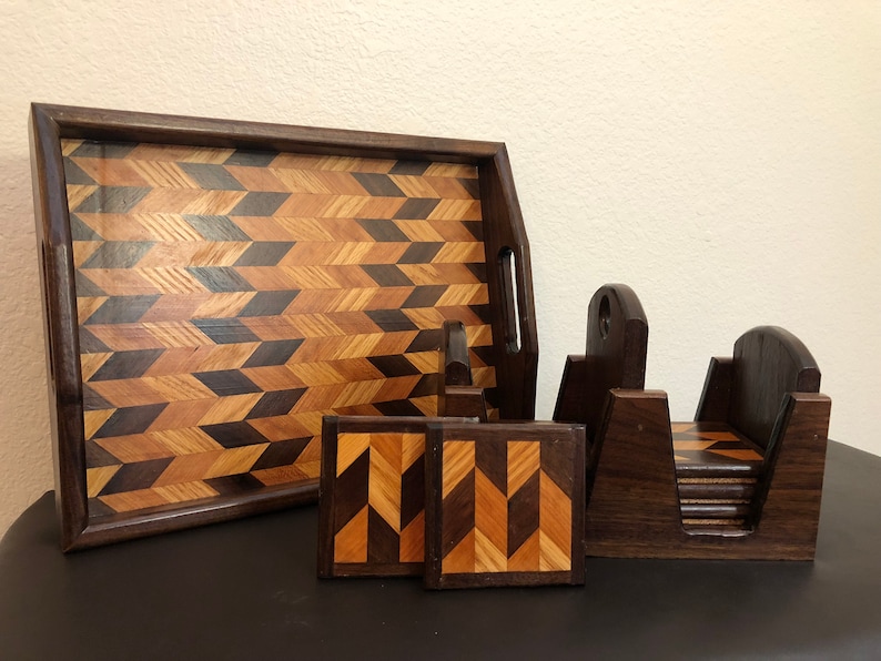May include: A set of wooden coasters and a serving tray with a geometric pattern made of different wood types. The coasters are stacked in a holder and the tray has two handles.