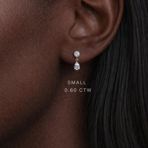 Puede incluir: Primer plano de una oreja con un peque&ntilde;o pendiente de diamantes. El pendiente tiene una parte superior redonda y una gota en forma de pera. El texto "SMALL 0.60 CTW" es visible.