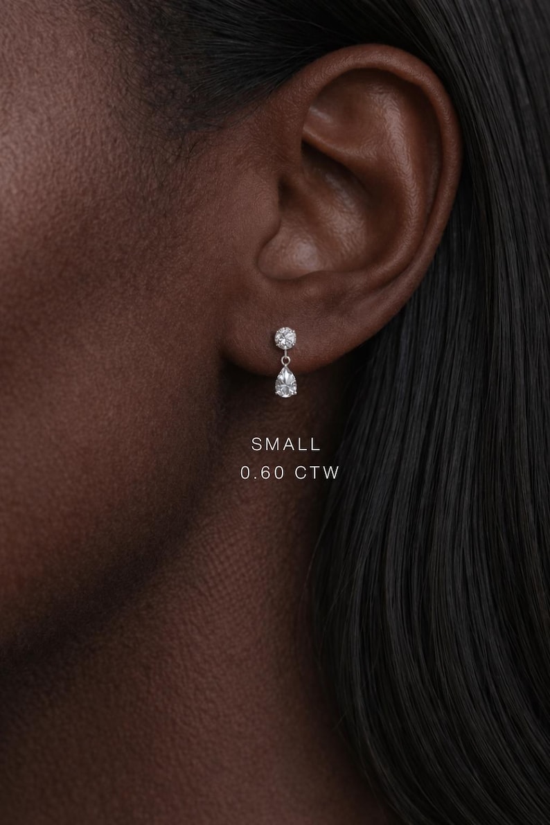 Puede incluir: Primer plano de una oreja con un peque&ntilde;o pendiente de diamantes. El pendiente tiene una parte superior redonda y una gota en forma de pera. El texto "SMALL 0.60 CTW" es visible.