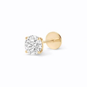 May include: A single gold stud earring with a round, clear diamond. The diamond is held in place by four prongs. The earring post and backing are also gold. The earring is set against a white background.