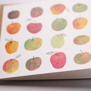 May include: A white card with a brown border features a pattern of 15 hand-painted apples in various shades of red, green, and yellow.