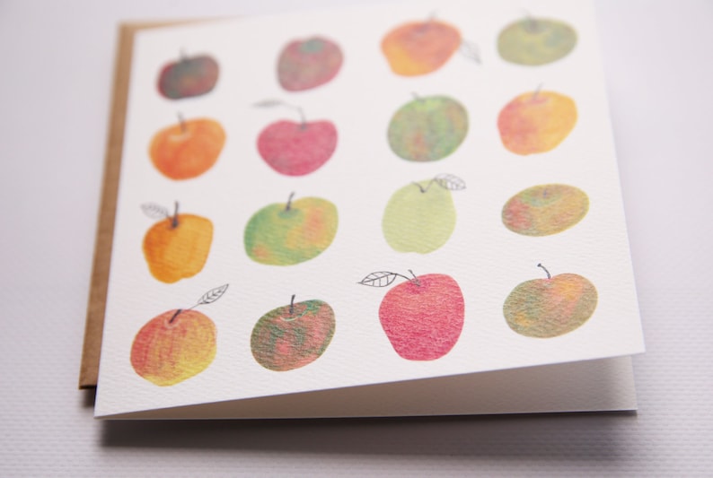 May include: A white card with a brown border features a pattern of 15 hand-painted apples in various shades of red, green, and yellow.