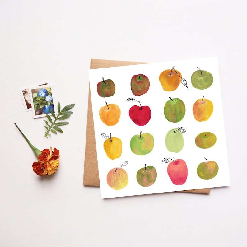 May include: A white card with a colorful illustration of 16 apples. The apples are painted in shades of red, green, yellow, and orange. The card is on a brown surface.
