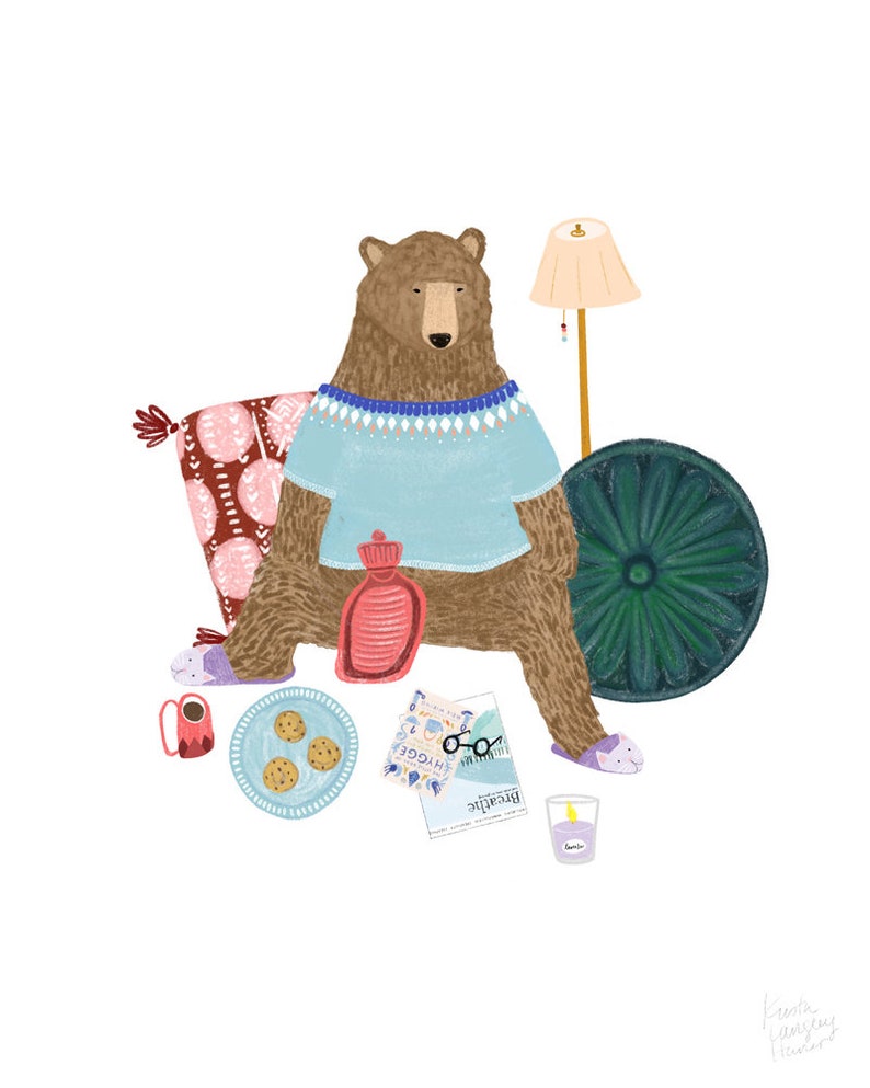 May include: A brown bear wearing a blue sweater and slippers sits on a pink and red patterned cushion. The bear is holding a red hot water bottle. There is a green round decorative object, a cup of coffee, a plate of cookies, a pair of glasses, a magazine titled "Breathe" and a glass of water on the floor.