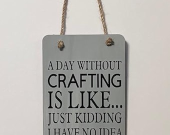 May include: A gray wooden sign with a white rope hanger. The sign reads "A day without crafting is like... Just kidding I have no idea."