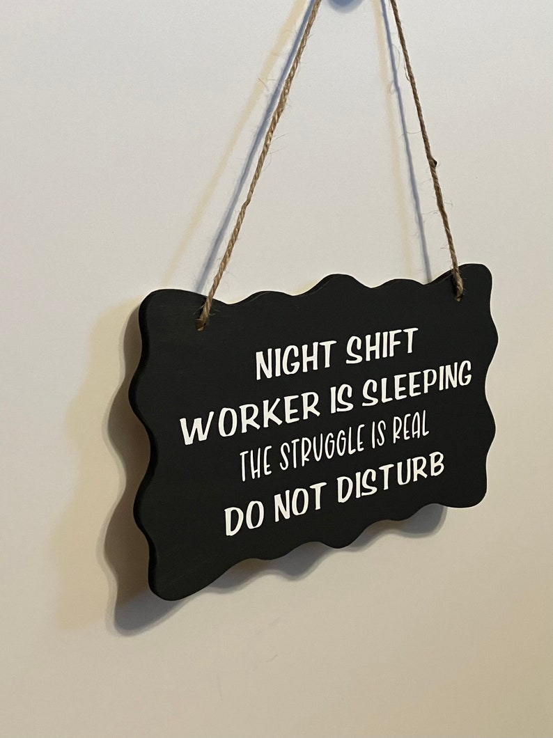 May include: Black sign with white text that reads "Night Shift Worker is Sleeping, The Struggle is Real, Do Not Disturb".