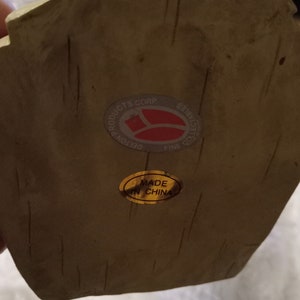 May include: Close-up of a beige collectible with a textured surface. It has a sticker reading "DELTON PRODUCTS CORP FINE COLLECTIBLES" and another sticker saying "MADE IN CHINA".