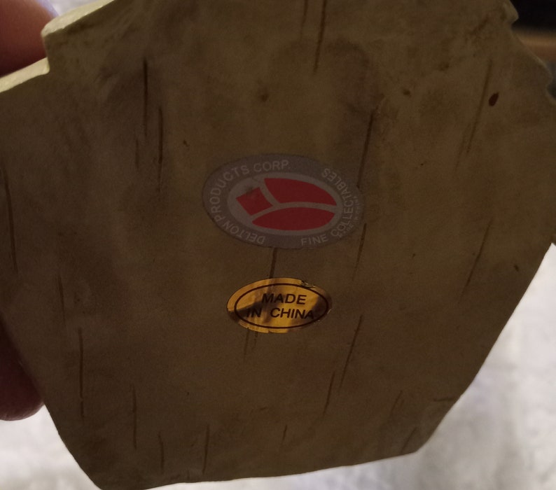 May include: Close-up of a beige collectible with a textured surface. It has a sticker reading "DELTON PRODUCTS CORP FINE COLLECTIBLES" and another sticker saying "MADE IN CHINA".
