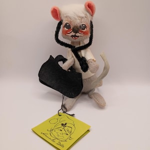 May include: A vintage Annalee Dolls mouse figurine, featuring a white head with pink ears, a black scarf, and a black bag. The mouse is holding a black bag and has a tag that says "Annalee Dolls".