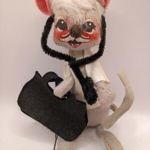May include: A vintage stuffed mouse doll dressed as a doctor, wearing a black stethoscope and holding a black bag. The mouse has a white head with pink ears and a painted face with rosy cheeks.