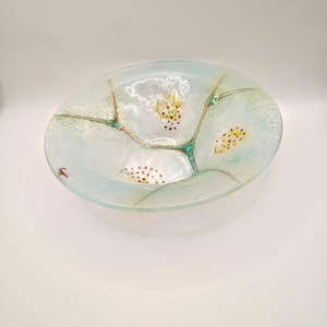 May include: Oval-shaped glass bowl with a light blue and white design. The bowl features a floral pattern with yellow and brown accents. The glass has a textured appearance, and the bowl is set against a white background.