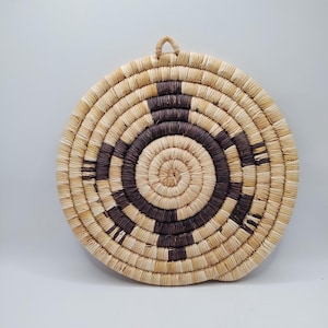 May include: A round woven wall hanging with a brown and tan pattern. The hanging is made of natural materials and has a rustic look.