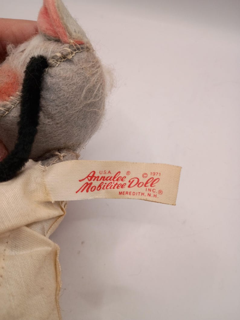 May include: A vintage Annalee Mobilitee Doll, featuring a gray head with pink ears and a black tail. The doll's tag reads "Annalee Doll, Meredith, N.H., USA, 1971". The doll is made of felt and fabric.