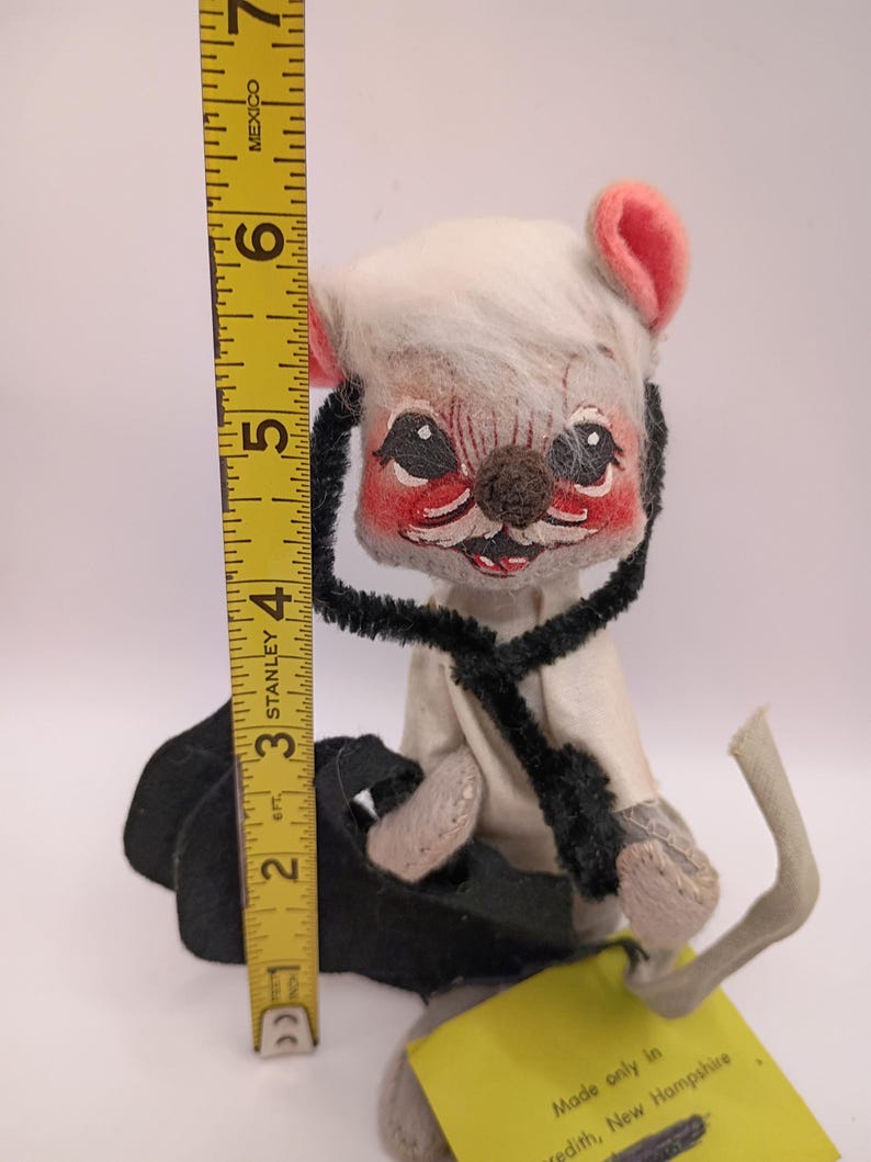 May include: A vintage stuffed mouse doll with a white head, pink ears, and a black pipe cleaner around its neck. The doll is approximately 6 inches tall. A yellow tag reads "Made only in Meredith, New Hampshire."