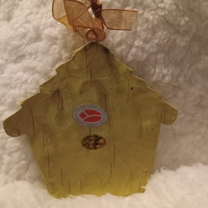 May include: A yellow birdhouse-shaped ornament with a textured surface and a gold ribbon for hanging. The ornament has a sticker that says "MADE IN CHINA". The birdhouse is a decorative item.