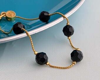 May include: A gold chain bracelet with five black faceted beads.