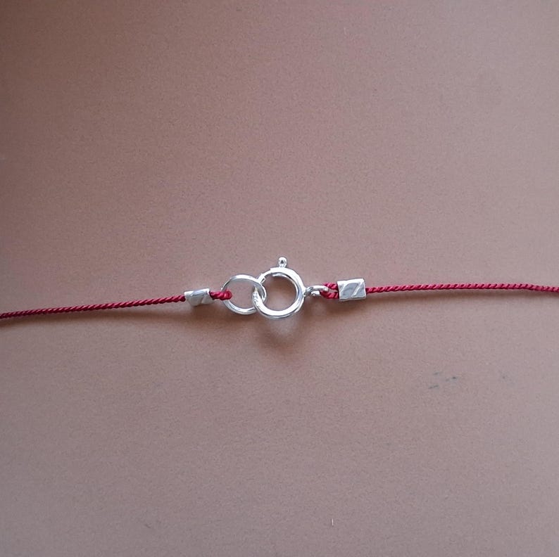 May include: A thin red cord necklace featuring a silver-toned spring ring clasp. The cord is secured at both ends by small silver-toned metal crimps that connect to the circular clasp mechanism, creating a simple and functional jewelry closure.