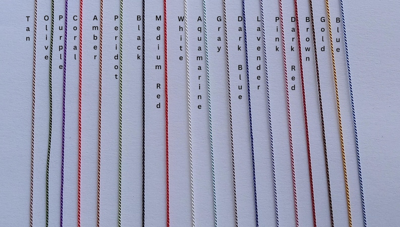 May include: A collection of fifteen vertical twisted cords in various colors, each labeled with text including Tan, Olive, Purple, Coral, Amber, Peridot, Black, Medium Red, White, Aquamarine, Gray, Dark Blue, Lavender, Pink, Dark Red, Brown, Gold, and Blue.